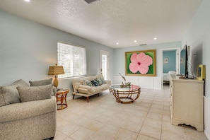 A living room with a beige sofa, a round table, and a large floral painting on the wall. - Coastal Escape w/ Yard Near Anna Maria Island (Bradenton)