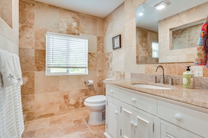 A bathroom with beige tiles, a toilet, a sink, and a mirror. - Coastal Escape w/ Yard Near Anna Maria Island (Bradenton)