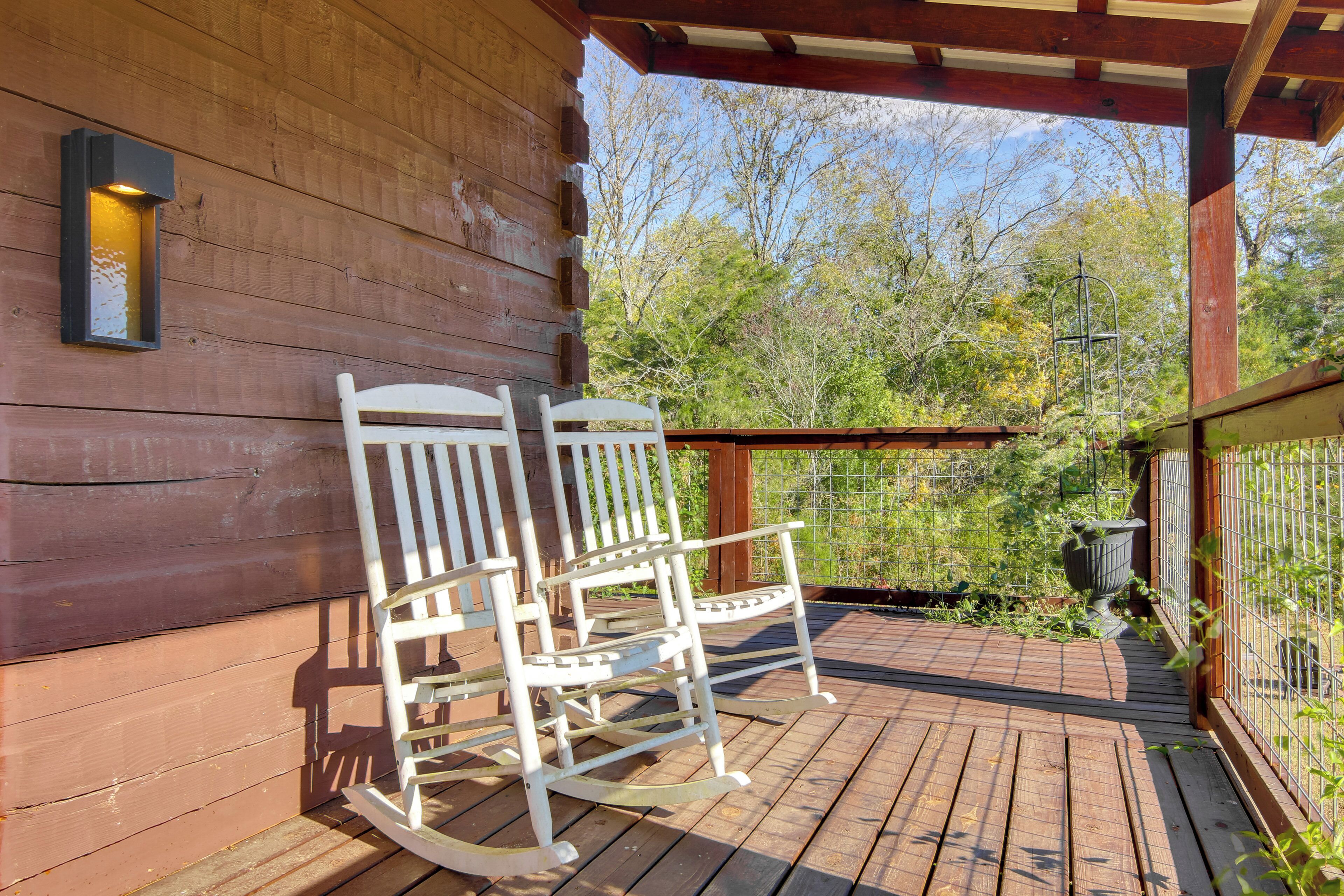 A wooden deck with two rocking chairs and a wall-mounted light fixture.