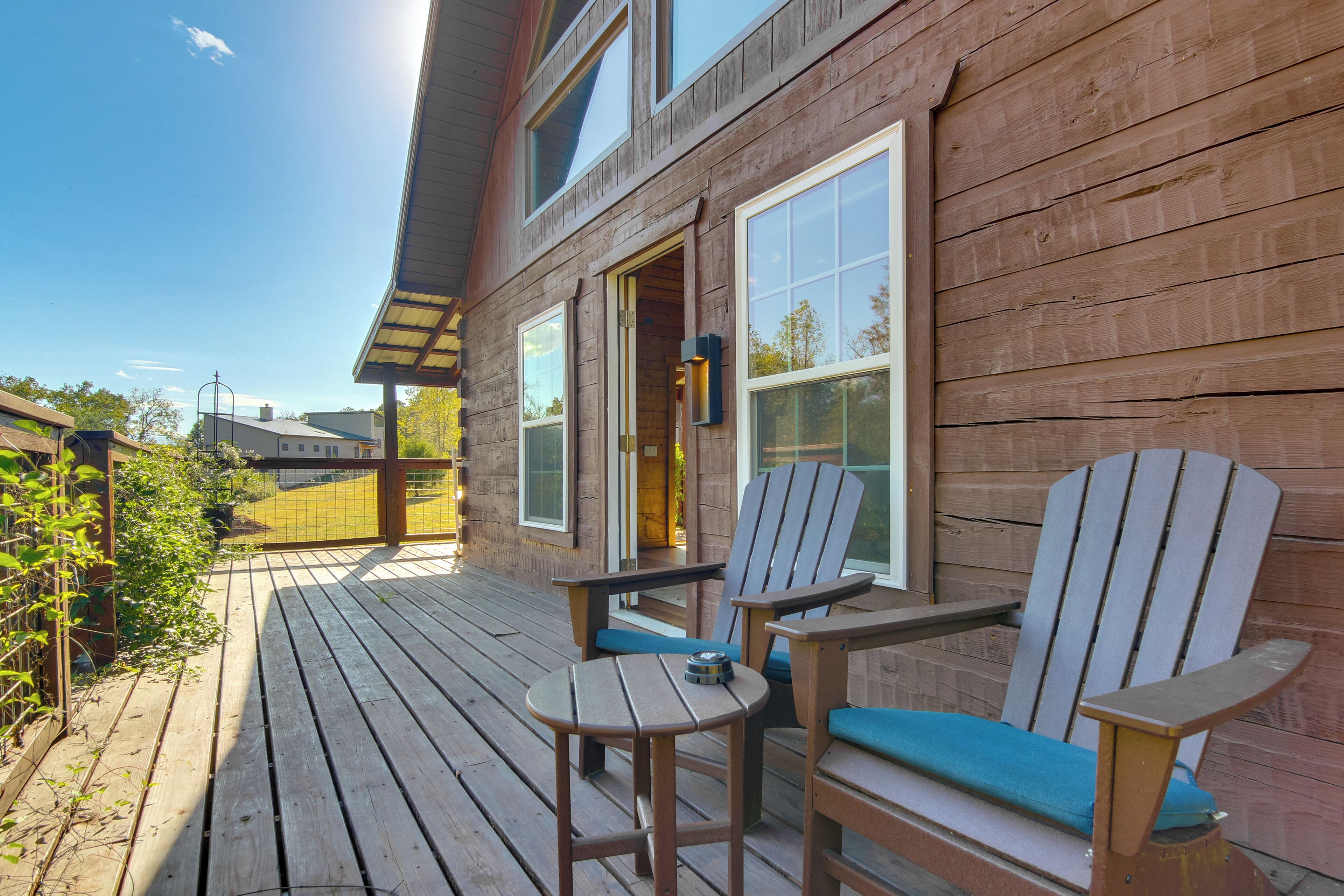 A wooden deck with two Adirondack chairs and a small table, a wooden house with large windows, and a clear sky.