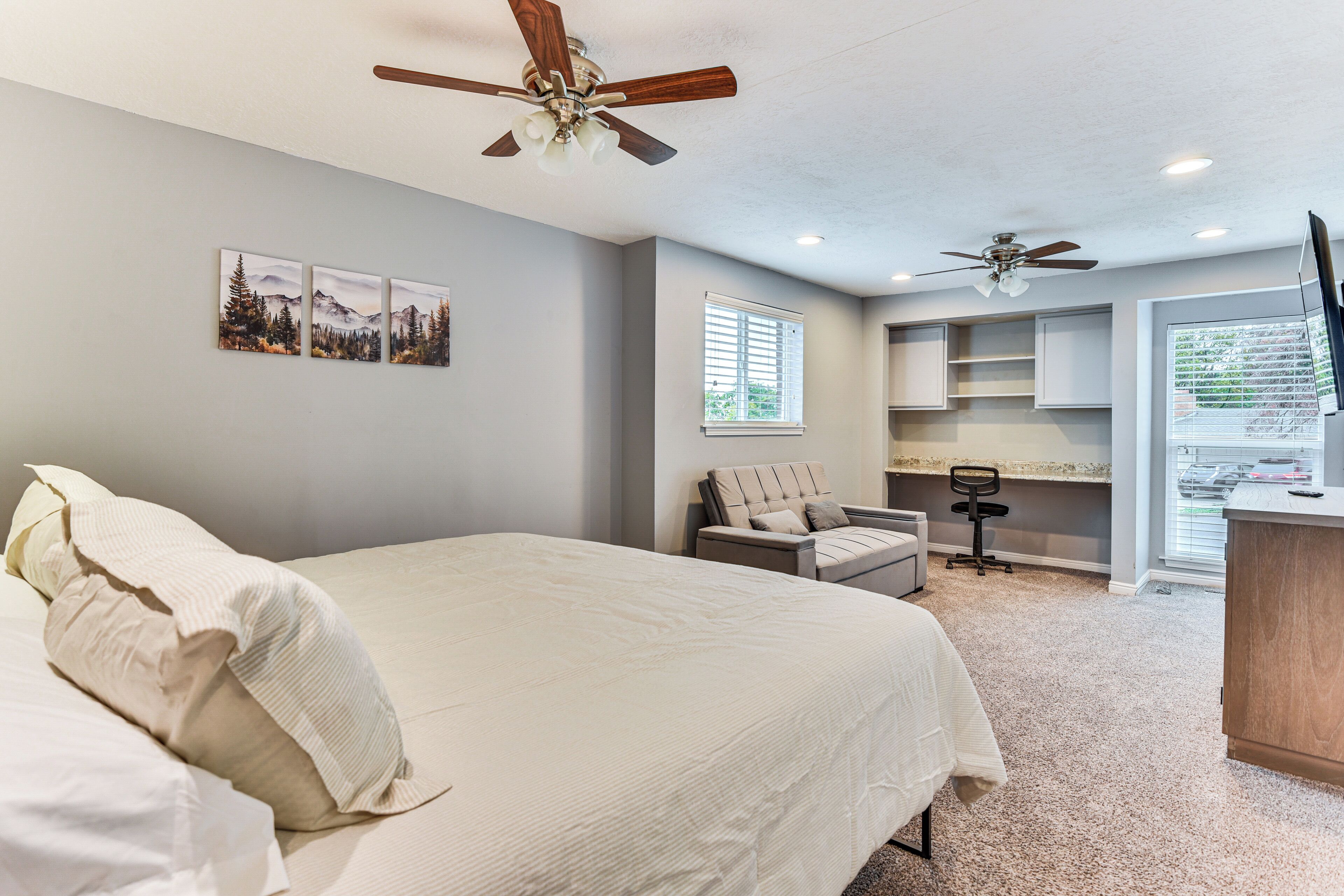 A bedroom with a large bed, a ceiling fan, a desk with a chair, and a TV.