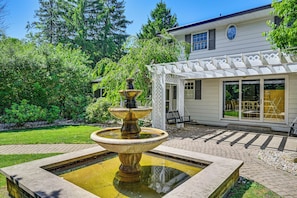Um jardim com uma fonte, um edifício branco com varanda coberta e um gramado.