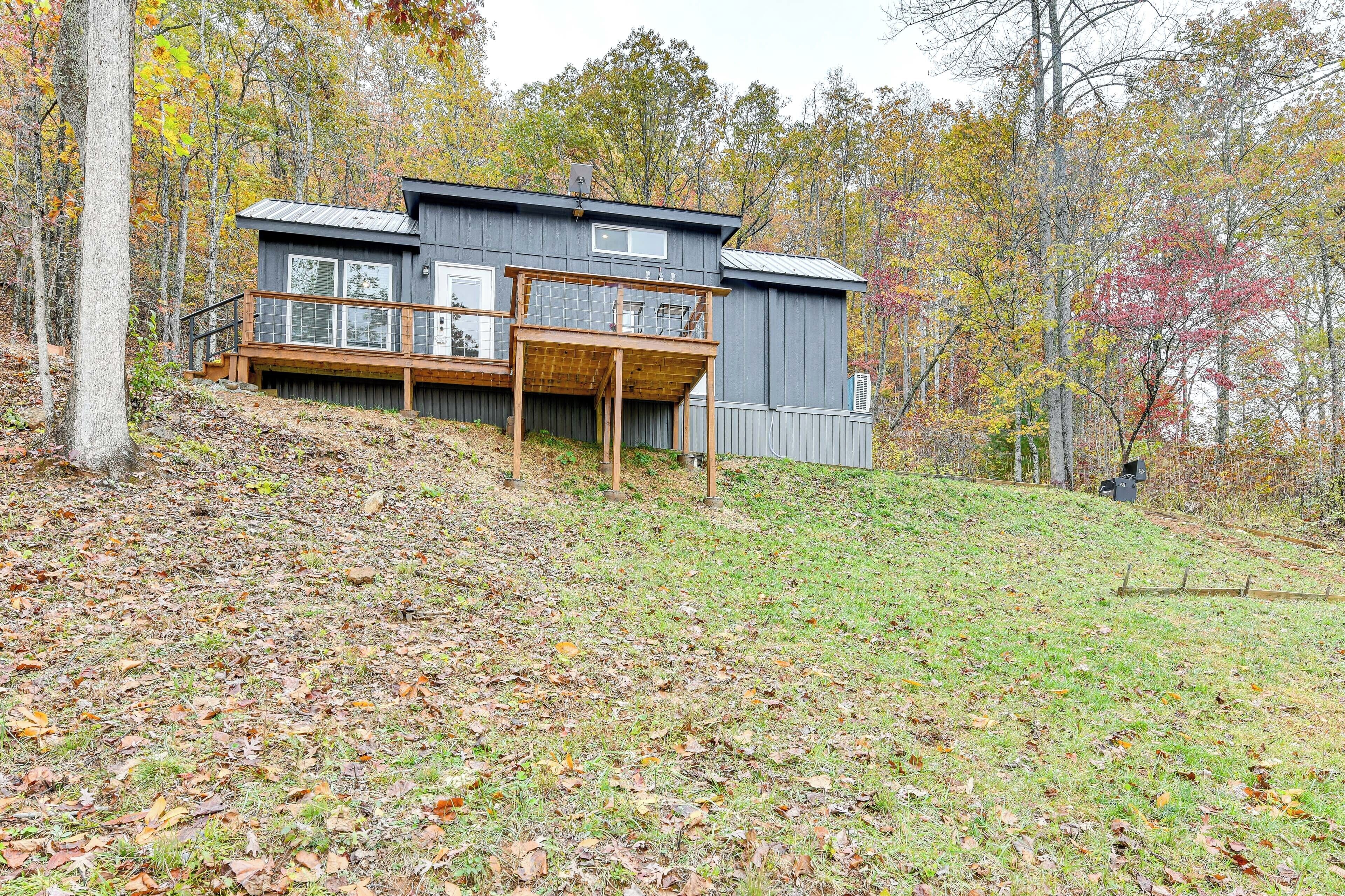 Eine moderne Hütte mit einer Holzterrasse, großen Fenstern und einem Metalldach, umgeben von Herbstlaub.