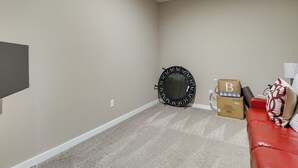Ein Zimmer mit beige gefärbten Wänden, einem roten Ledersofa, einem schwarzen, runden Gegenstand und Kartons.