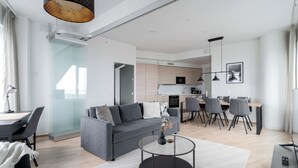 A modern living room with a grey sofa, a dining area with a table and chairs, a kitchen in the background, and a staircase leading to another level. - 12th Floor Sauna Retreat with Views (Tampere)