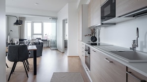 A modern kitchen with a microwave, sink, and wooden cabinets. There is a dining area with a table and chairs. - 12th Floor Sauna Retreat with Views (Tampere)