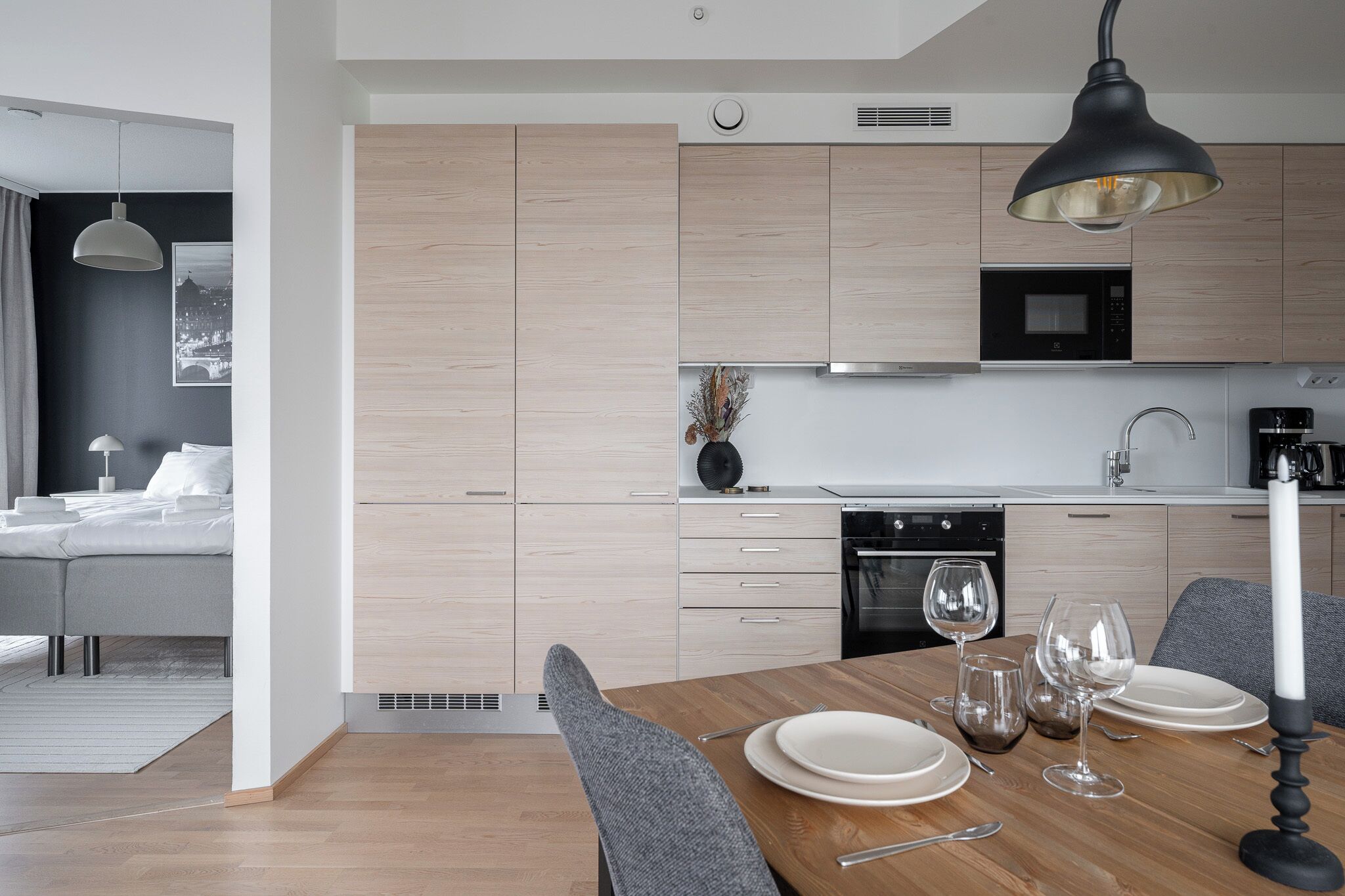 Een moderne keuken met lichte houten kastjes, een magnetron en een eethoek met een tafel voor vier personen.