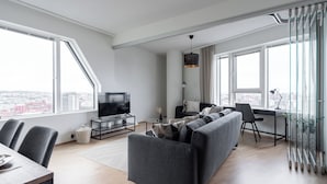 A modern living room with a sofa, TV, dining table, and large windows offering a city view. - 12th Floor Sauna Retreat with Views (Tampere)