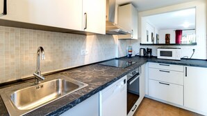 A modern kitchen with a stainless steel sink, white cabinets, a black marble countertop, and a built-in dishwasher. - Beautiful apartment, 10 minutes walk from the beach (Urbanización Estrella de la Bahía)