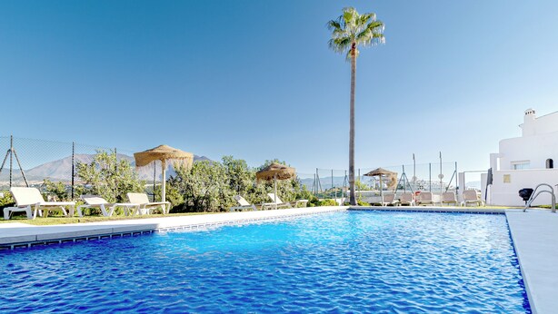 A swimming pool with lounge chairs and palm trees, surrounded by a fence and white buildings. - Beautiful apartment, 10 minutes walk from the beach (Urbanización Estrella de la Bahía)