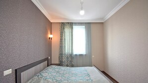 Ein Schlafzimmer mit einem Bett, einem fensterbelaubten Fenster, einer Wandleuchte und einer Deckenlampe.
