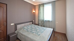 Ein Schlafzimmer mit einem Bett, einem Nachttisch, einer Wandleuchte, einem Fenster mit Vorhängen und einer Tür.