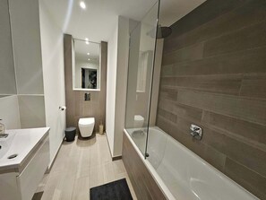 Ein modernes Badezimmer mit einer Duschkabine, einer weißen Toilette und einer Badewanne.