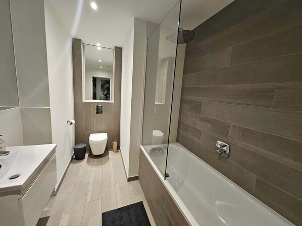 Ein modernes Badezimmer mit einer Duschkabine, einer weißen Toilette und einer Badewanne.