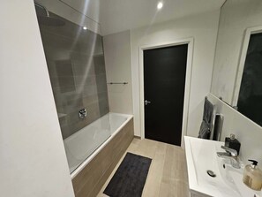Ein modernes Badezimmer mit Duschkabine, Badewanne, Waschbecken und Spiegel sowie einer Tür.