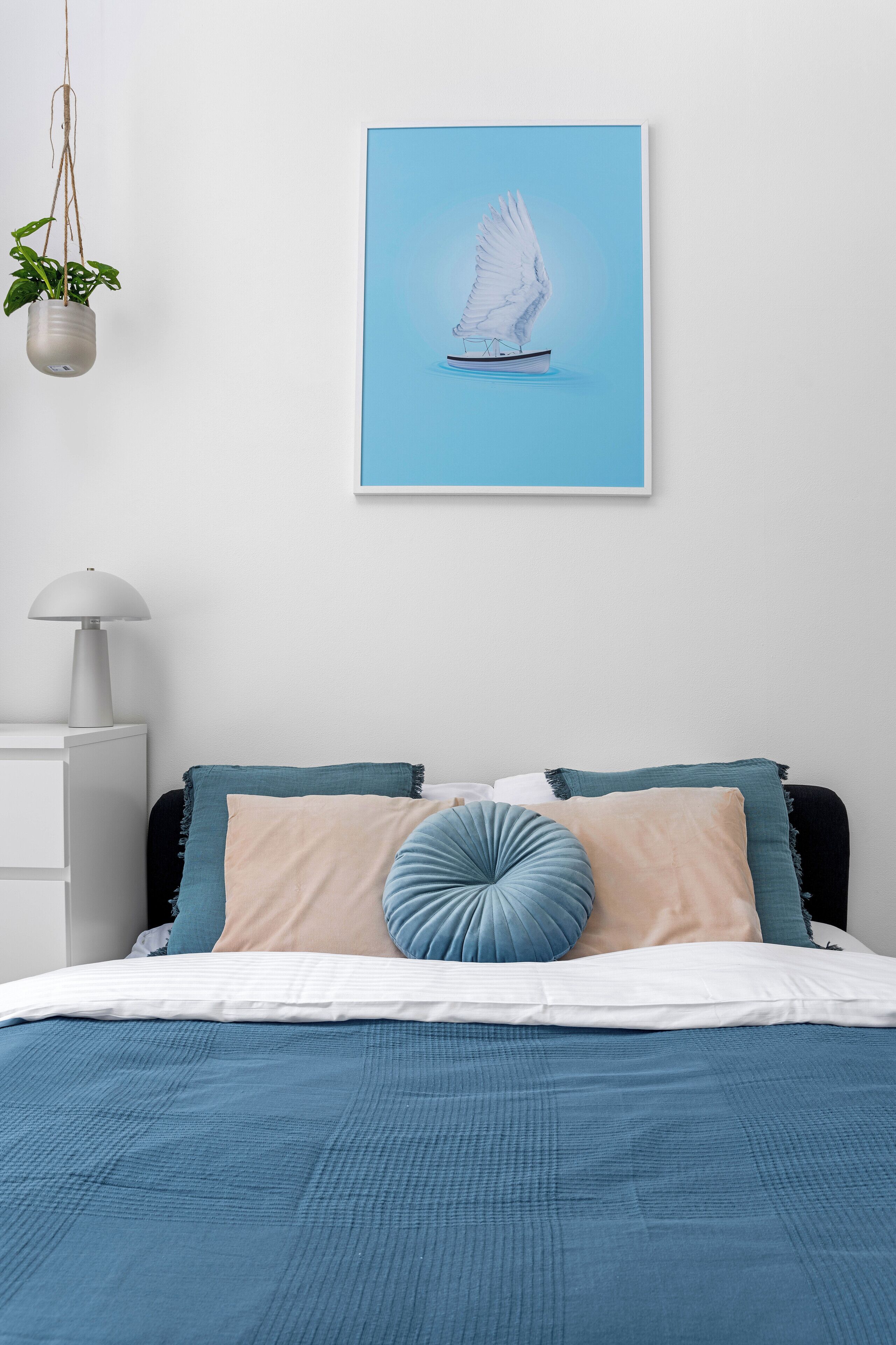 A bedroom with a bed, a hanging plant, a lamp, and a framed picture on the wall.