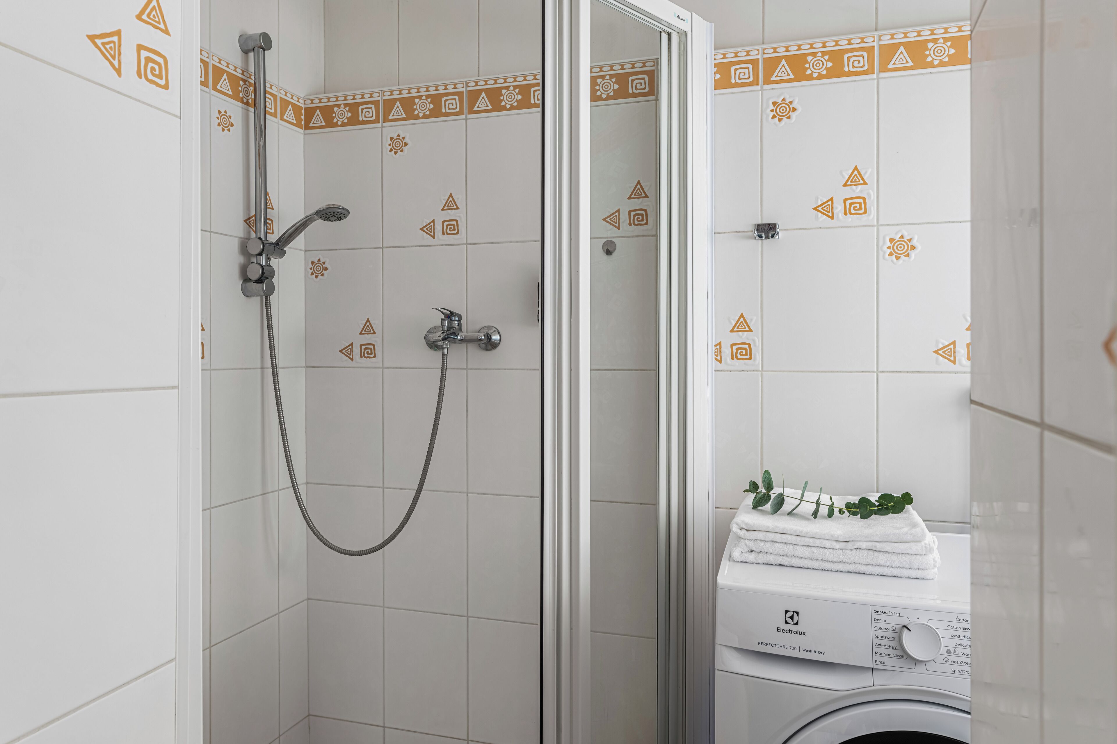A bathroom with a shower, a washing machine, and patterned tiles.