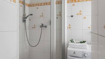 A bathroom with a shower, a washing machine, and patterned tiles.