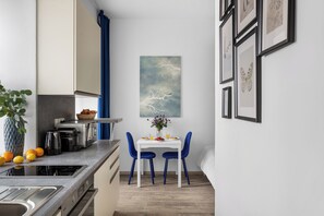 A modern kitchen with a dining area, featuring a white table, blue chairs, and a blue curtain. - Enjoy Downtown Boutique Apartments #12 by Goodnite cz (Brno)