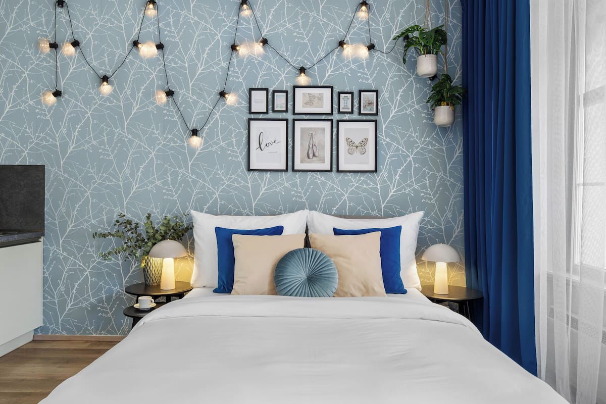 A bedroom with a bed, bedside tables, wall art, and string lights.