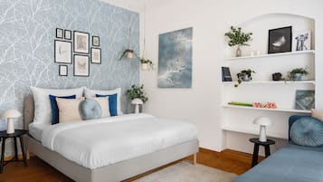 A modern bedroom with a bed, bedside tables, a wall with framed pictures, and shelves with plants and decorative items.