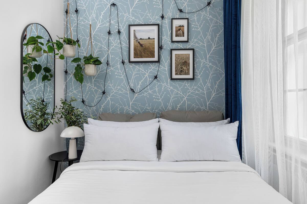 A bedroom with a bed, white pillows, a round mirror, and wall-mounted plants.