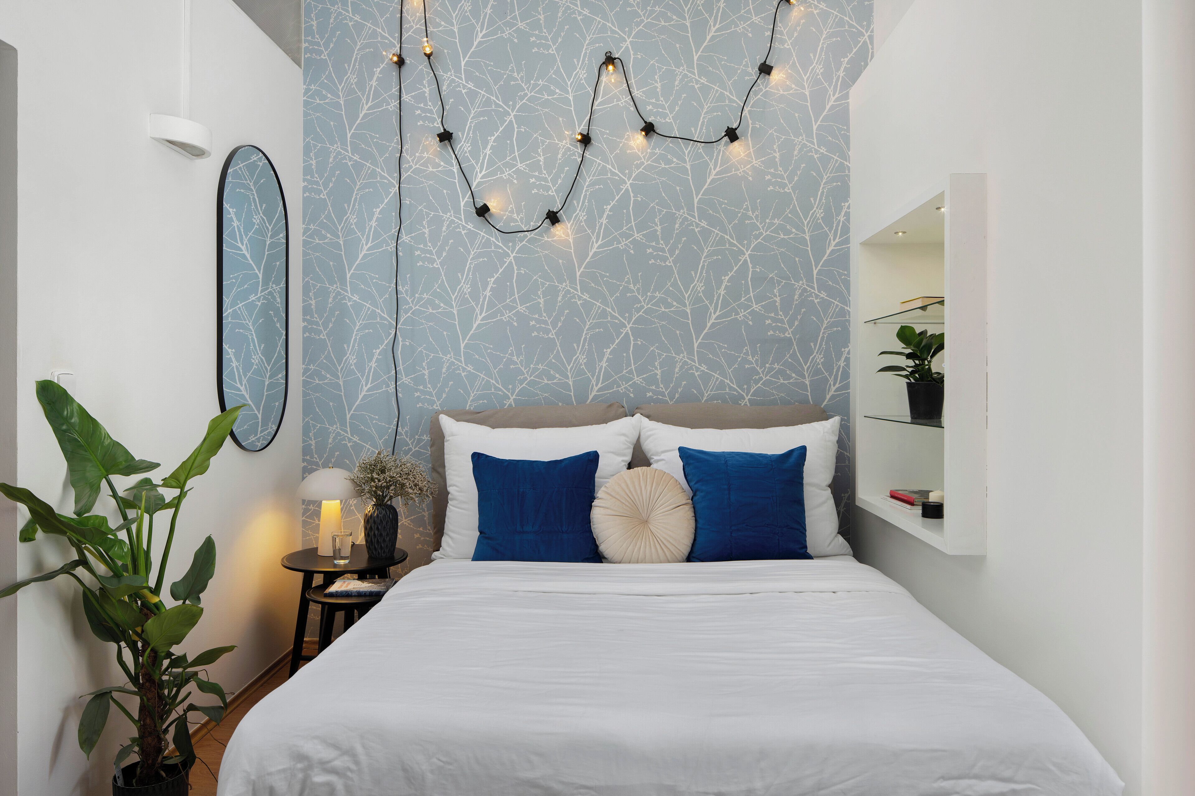 A modern bedroom with a bed, blue pillows, a nightstand, a lamp, and a string of lights.