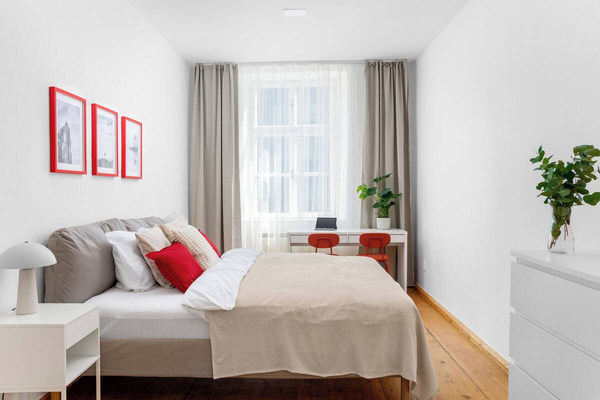 A bedroom with a bed, a desk, and a chair. There are three framed pictures on the wall.