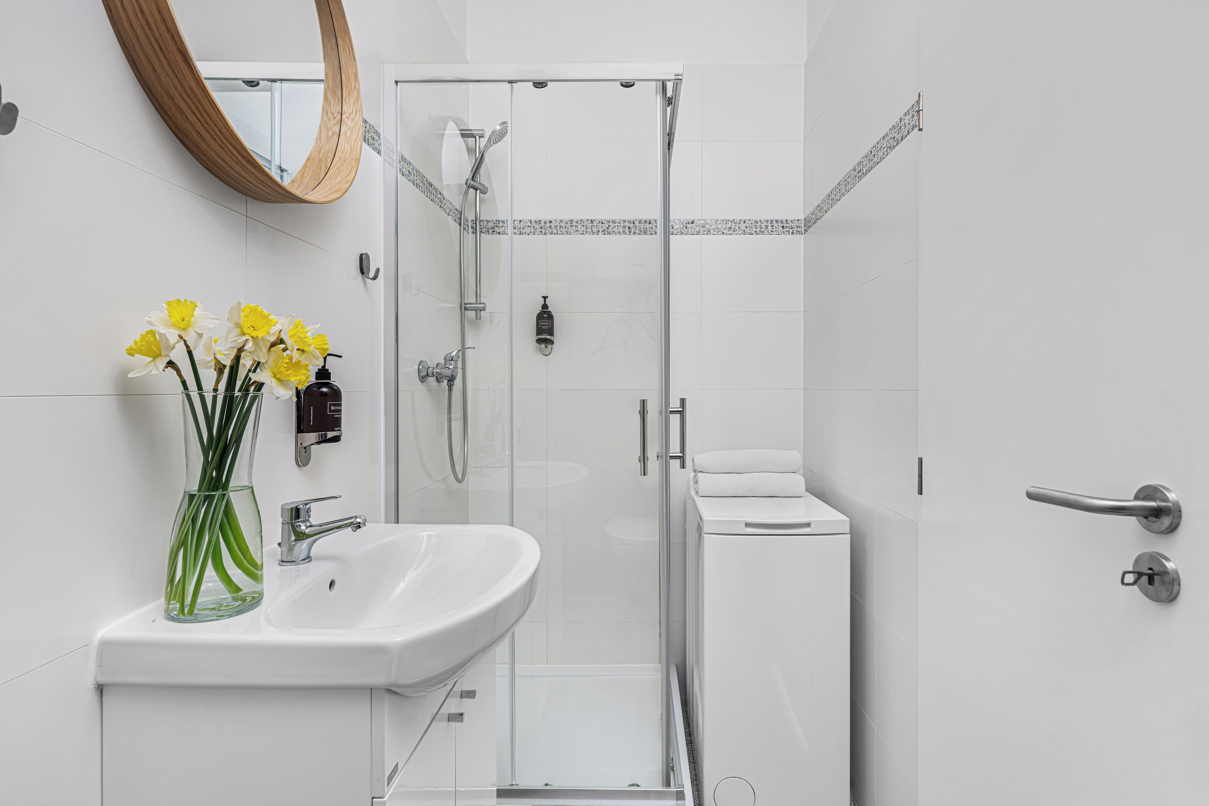 Une salle de bain moderne avec un lavabo blanc, une cabine de douche en verre et un miroir avec un cadre en bois.