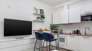 A modern kitchen with white cabinets, a flat-screen TV, two blue bar stools, and a wooden countertop. - Enjoy Downtown Boutique Apartments #12 by Goodnite cz (Brno)