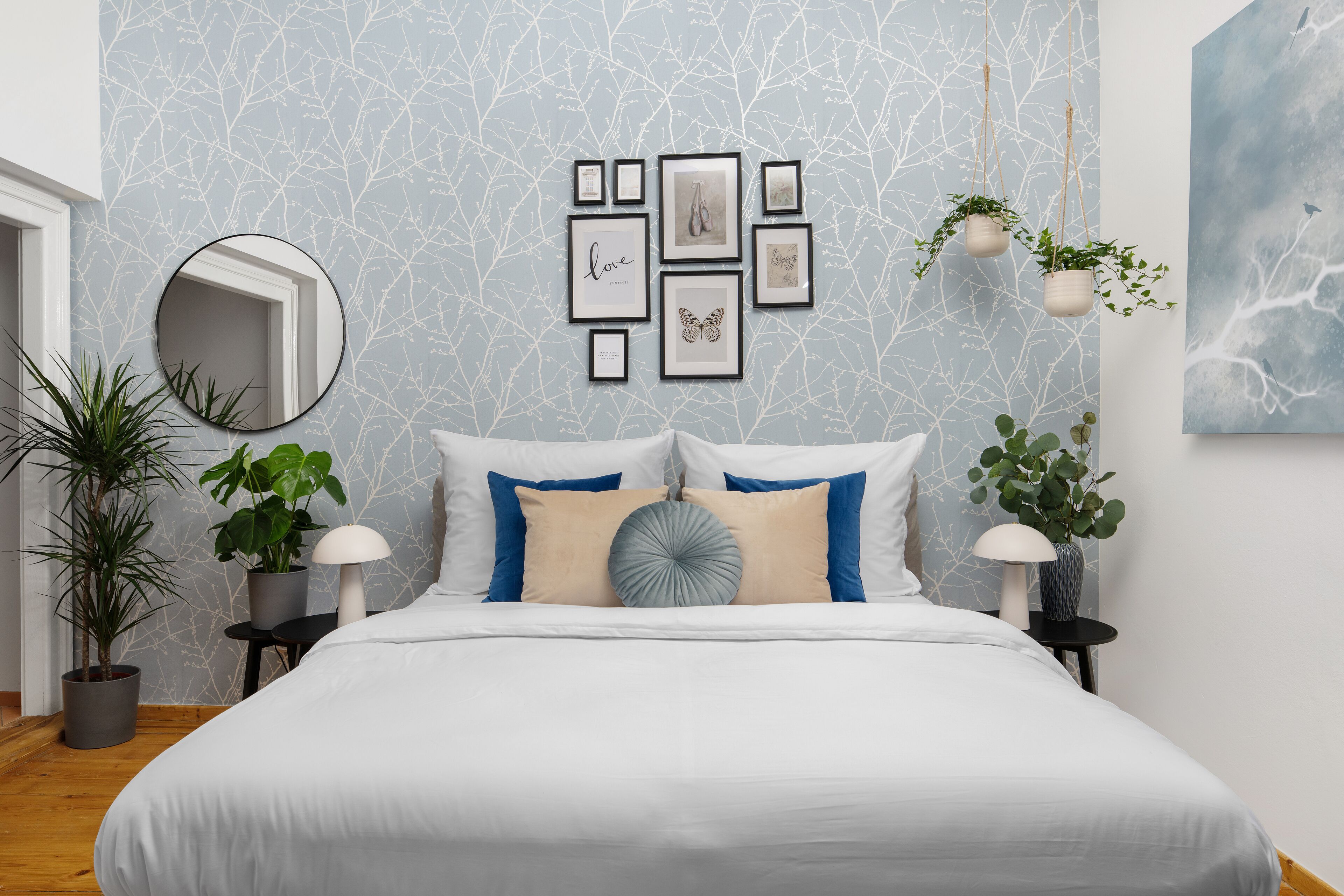 Un dormitorio con cama, cuadros enmarcados y plantas colgantes.