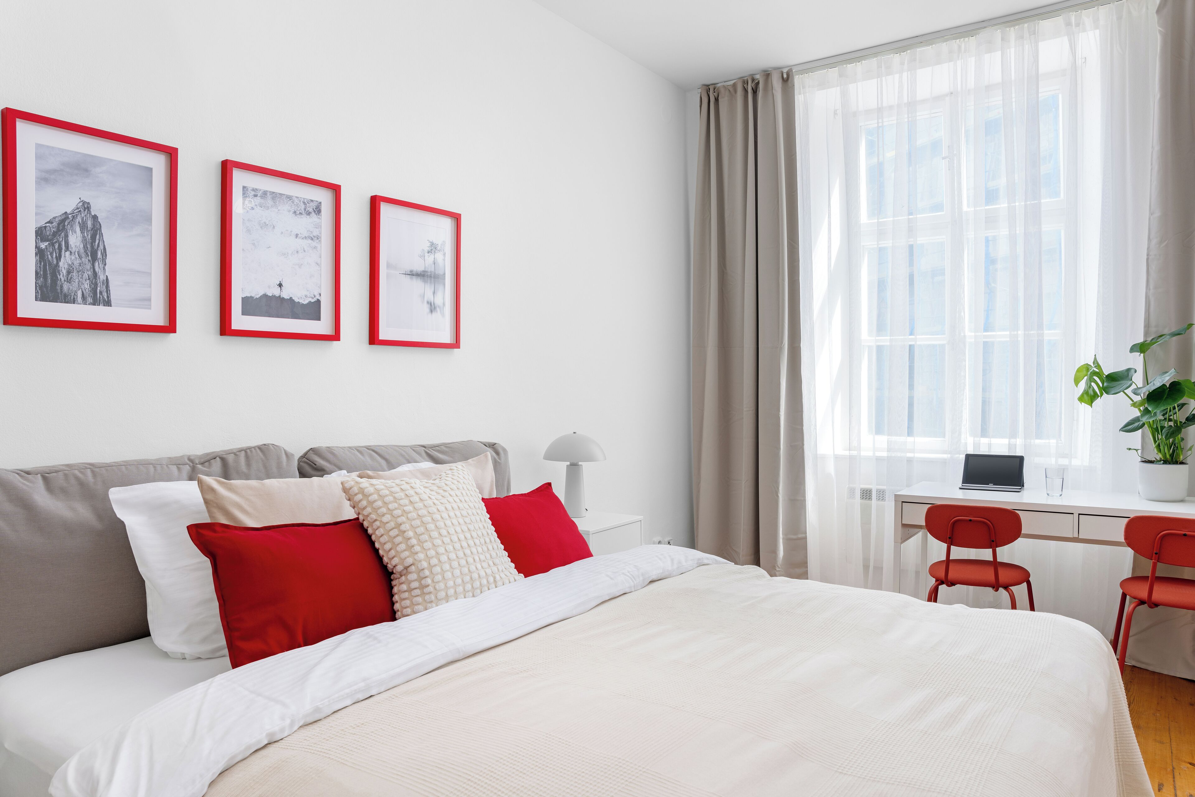 A modern bedroom with a bed, a desk with a laptop, and a window with curtains.