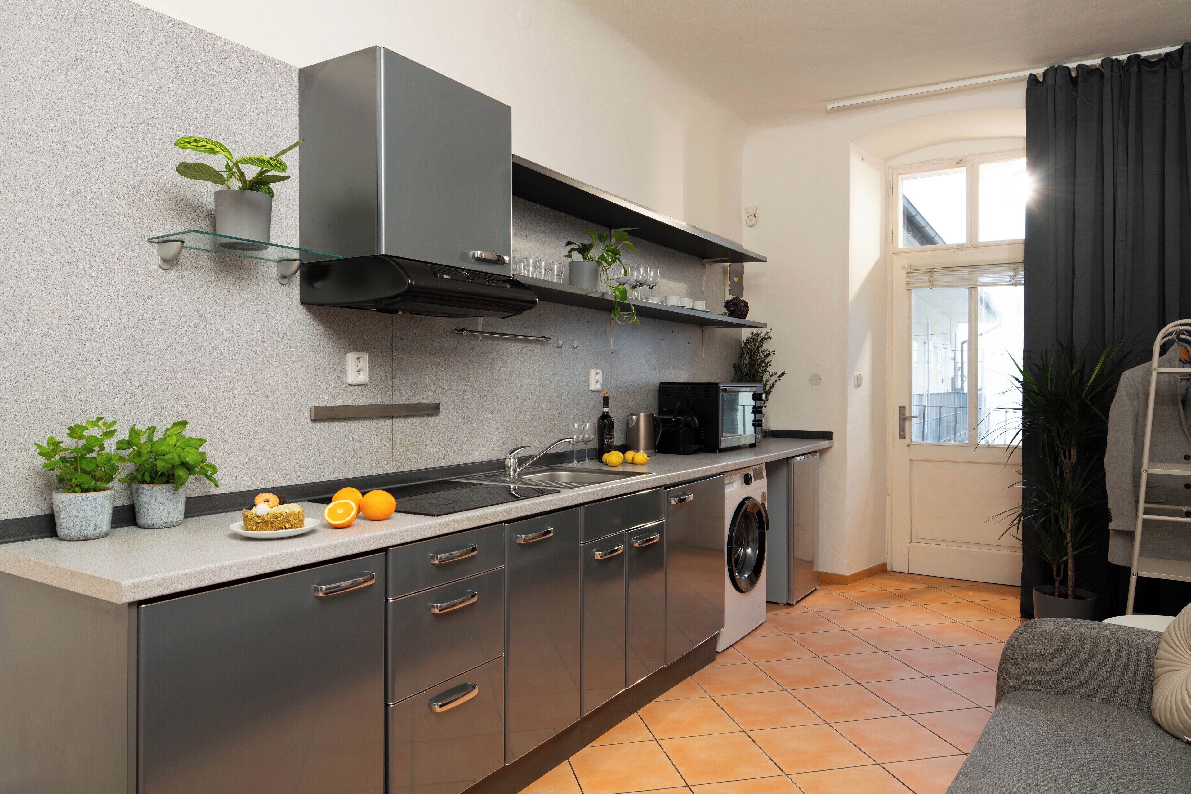 Eine kompakte Küche mit Einbauofen, Waschmaschine und Essbereich mit grauem Sofa.