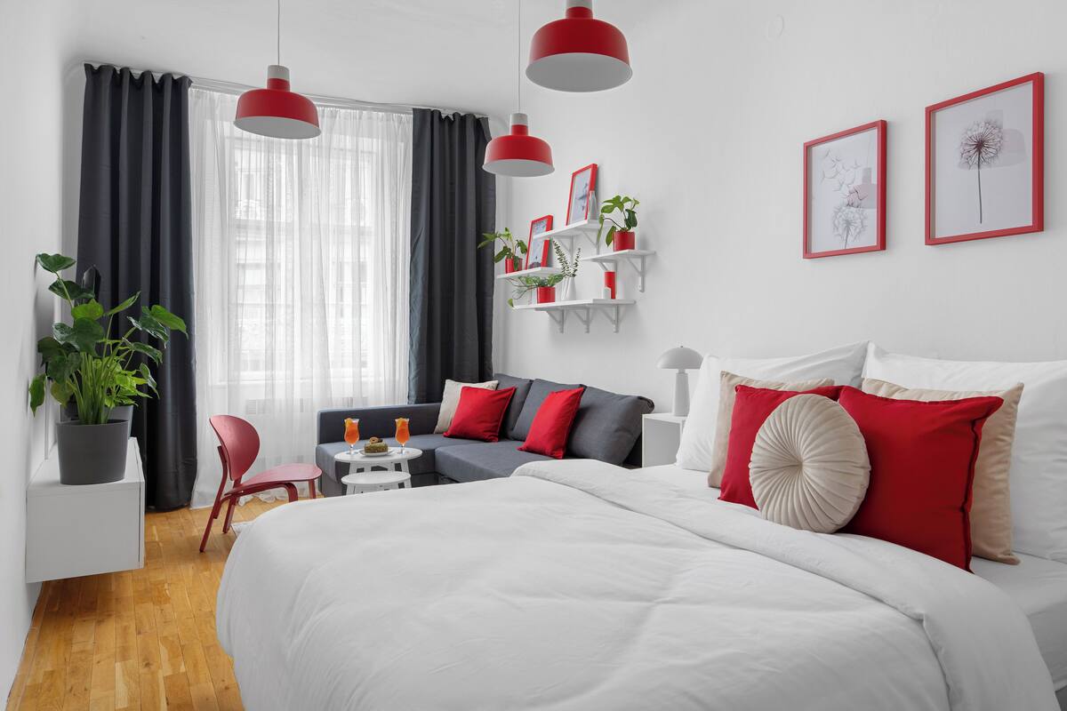 A modern hotel room with a large bed, a sofa, a small table, and a potted plant.