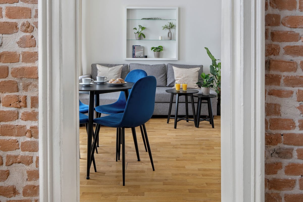 A room with a brick wall, a white door, a dining table with chairs, and a sofa.