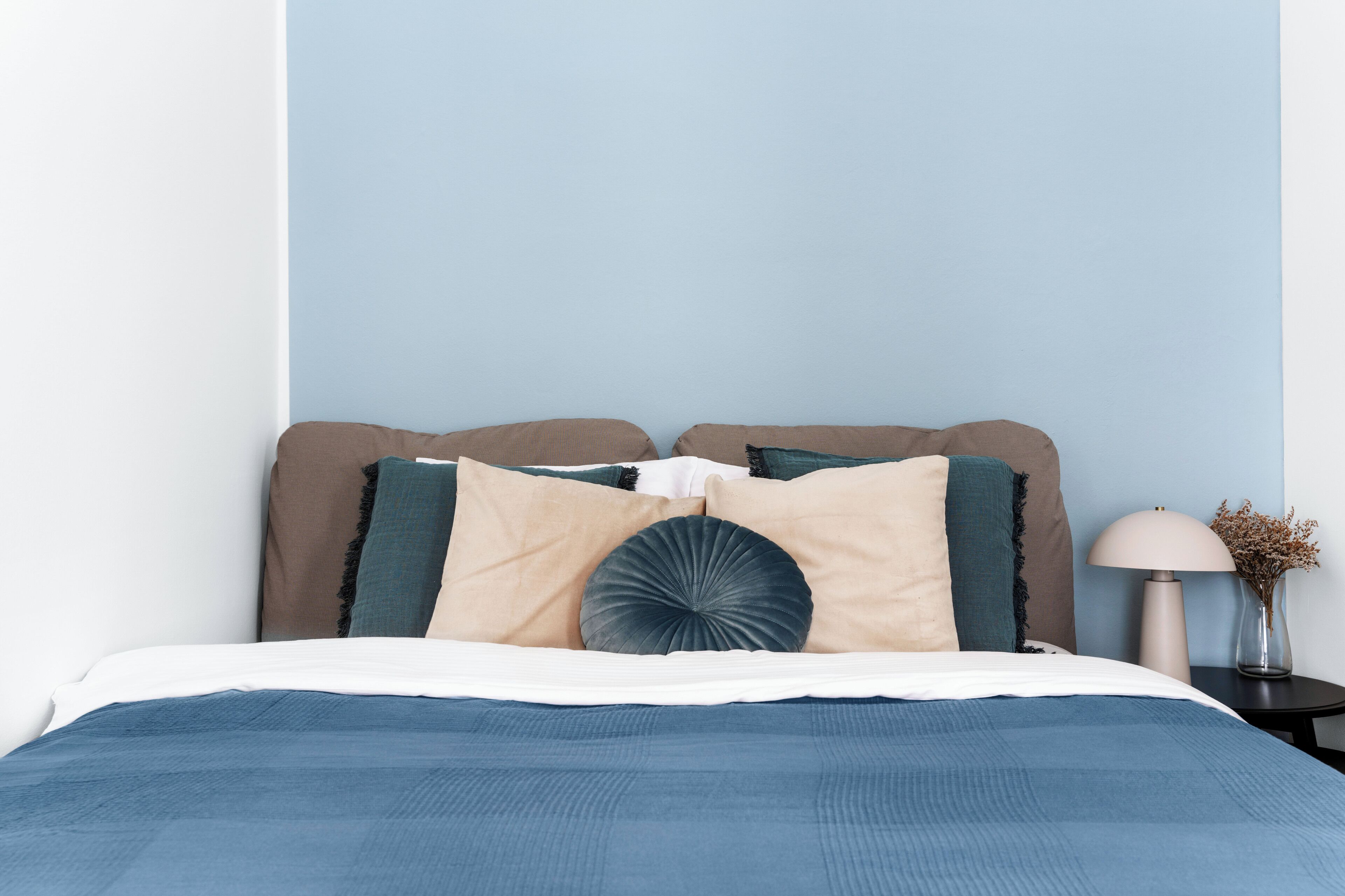 Una cama bien hecha con cubrecama azul, almohadas color beige y azul, y un cojín decorativo.