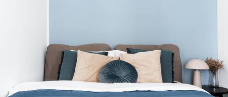 Una cama bien hecha con cubrecama azul, almohadas color beige y azul, y un cojín decorativo.