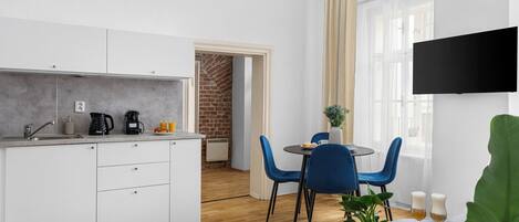 A modern kitchen with white cabinets, a brick wall, and a dining area with blue chairs and a small table.