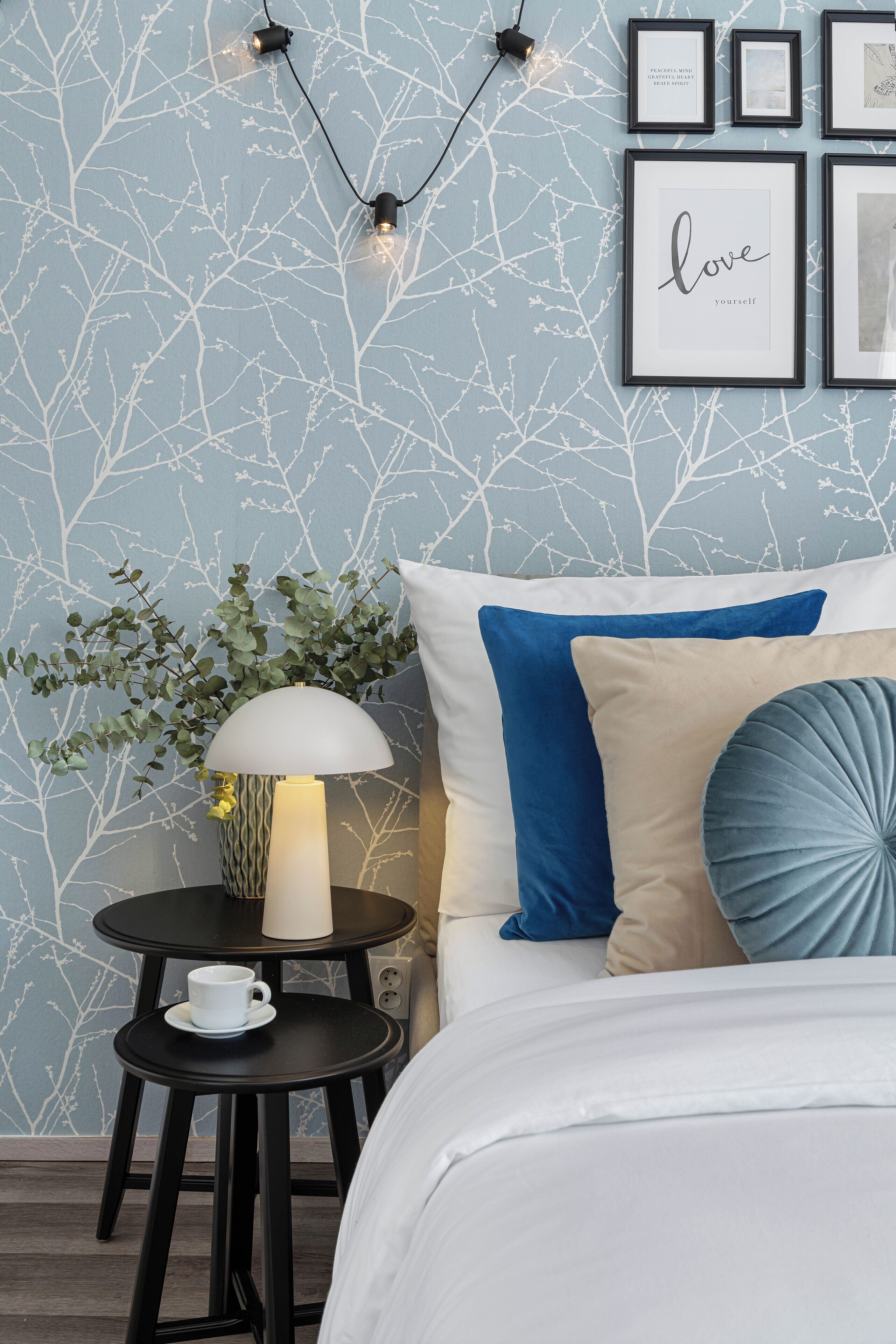 A neatly arranged bedroom with a bed, bedside table, lamp, and framed pictures on the wall.