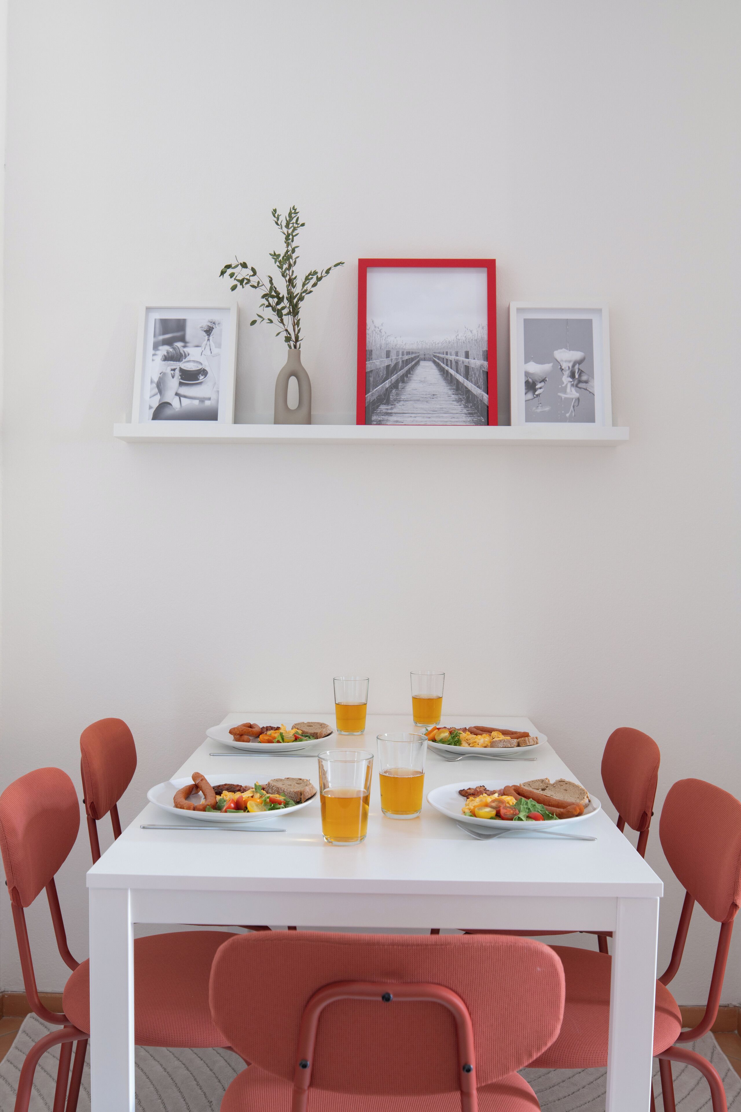 Une table à manger, dressée avec des assiettes de nourriture et des boissons, entourée de chaises rouges.