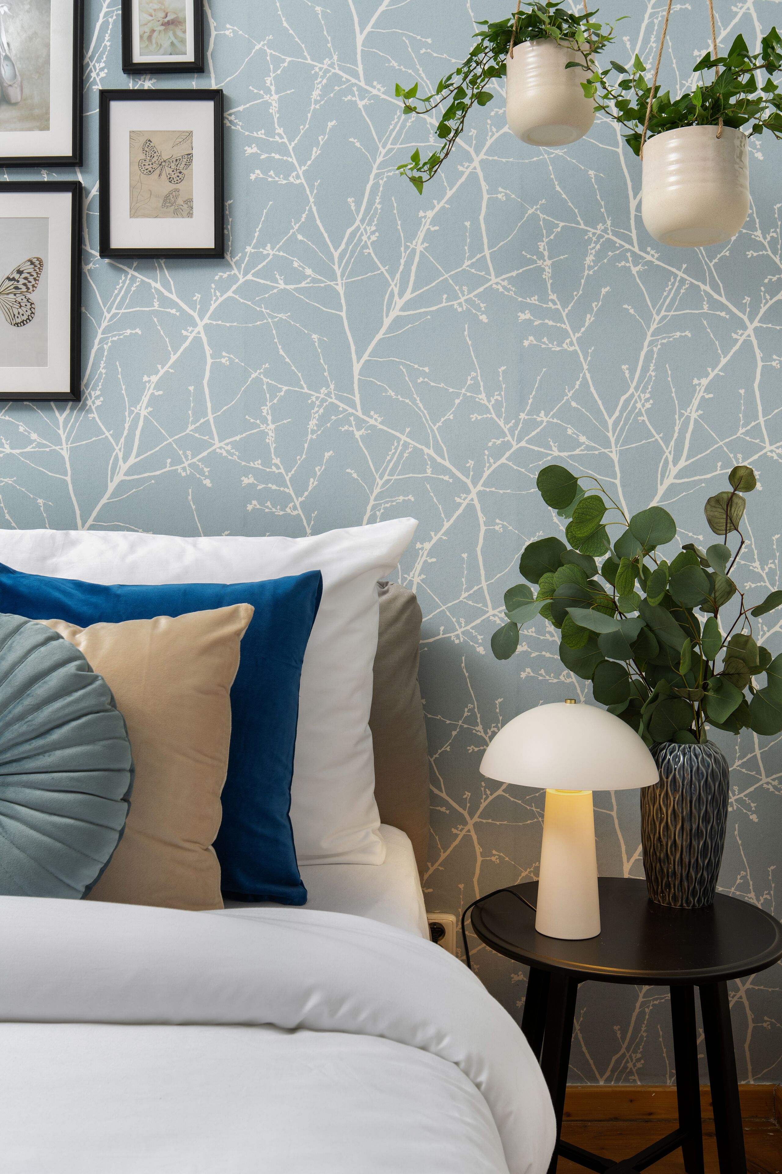 A bedroom with a bed, pillows, a bedside table with a lamp, and wall-mounted planters.