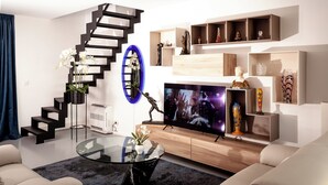 A modern living room with a black spiral staircase, a flat-screen TV, and a variety of decorative items on shelves. - Suite Aux Anges (Antwerp)