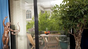 A balcony with a statue, wooden chairs, a table with fruit, and a potted plant. - Suite Aux Anges (Antwerp)
