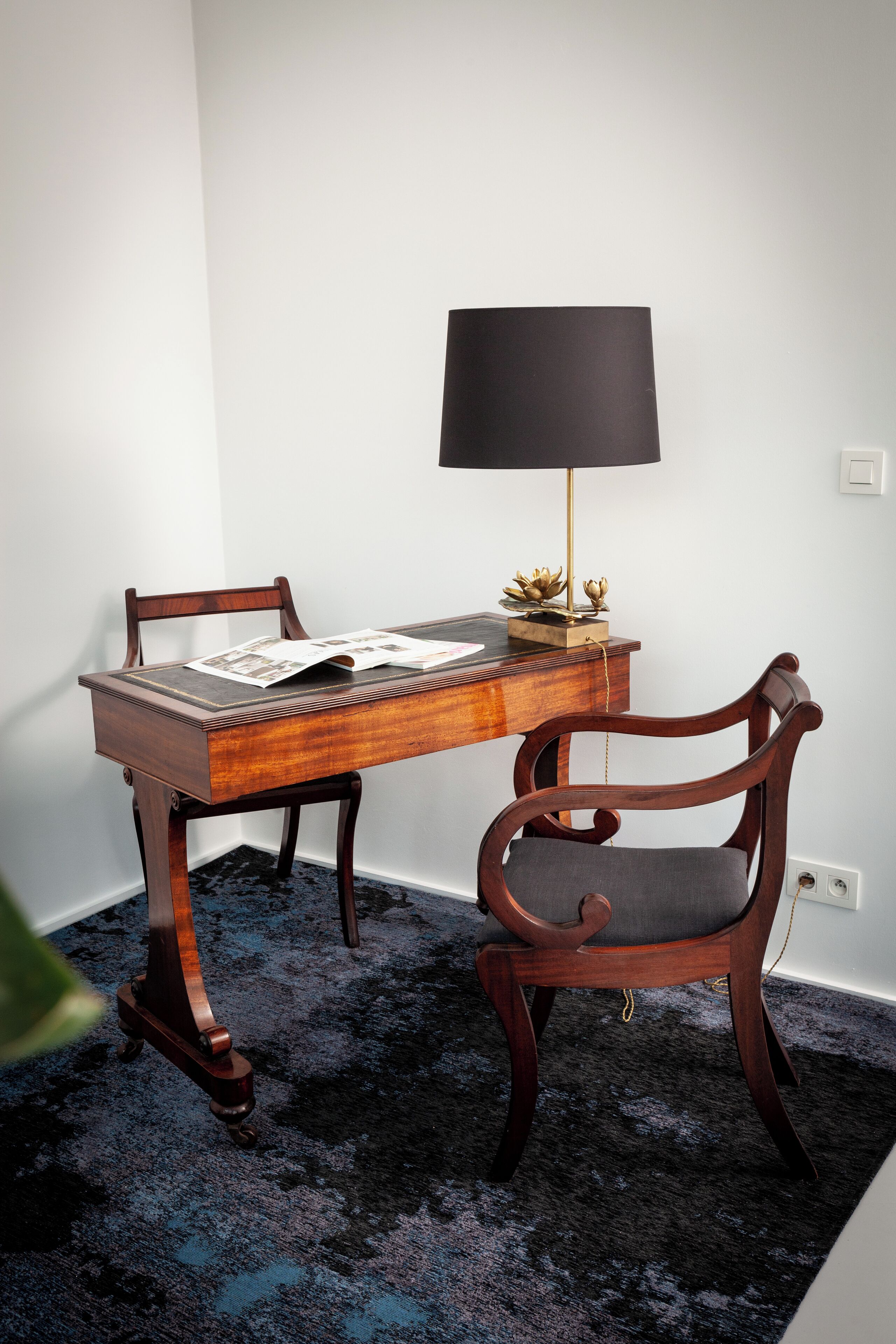 A wooden desk with a lamp, two chairs, and a carpeted floor.