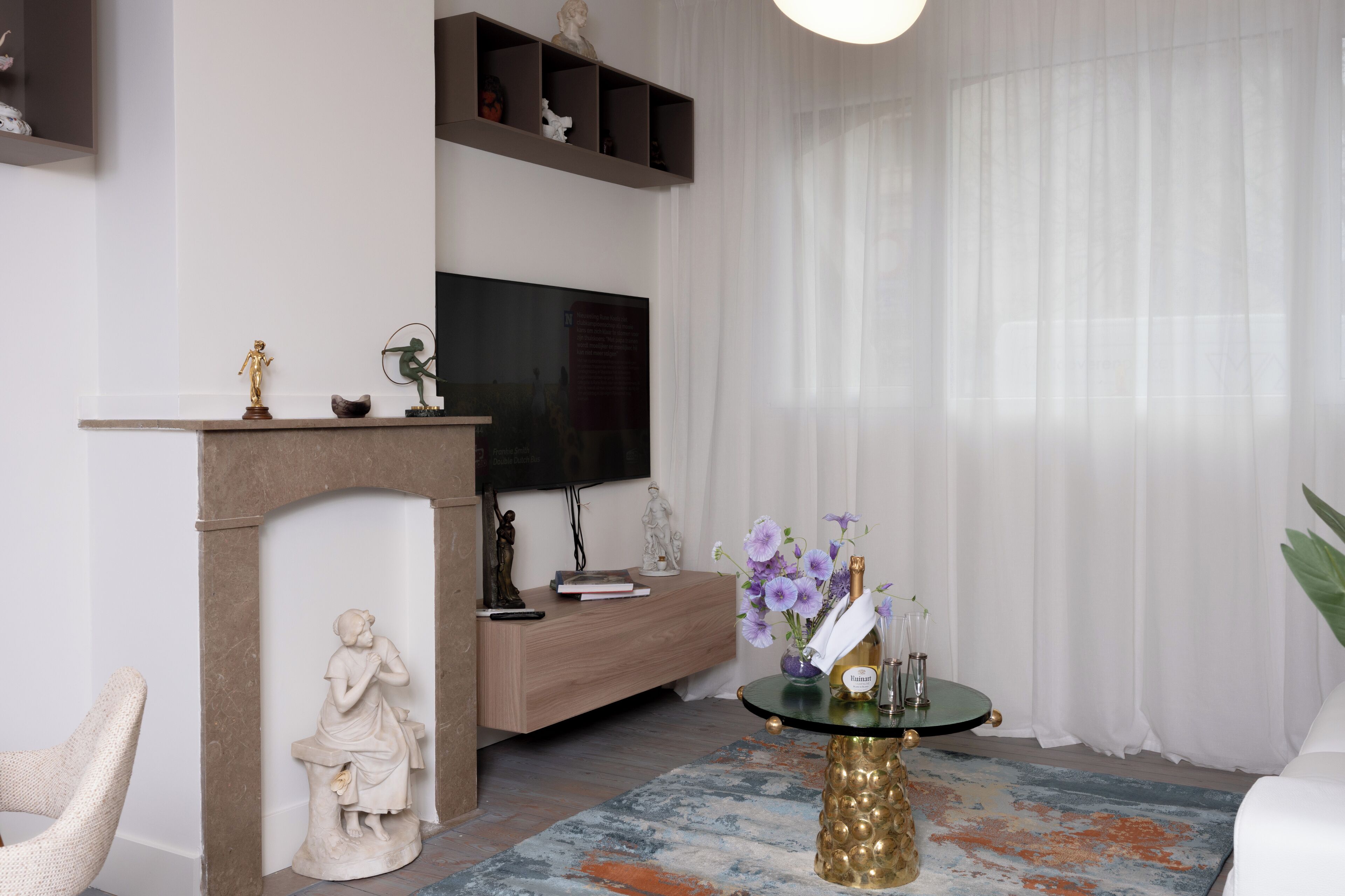Un salon avec une cheminée, un téléviseur fixé au mur, une table basse ronde ornée d’un vase de fleurs et un canapé.
