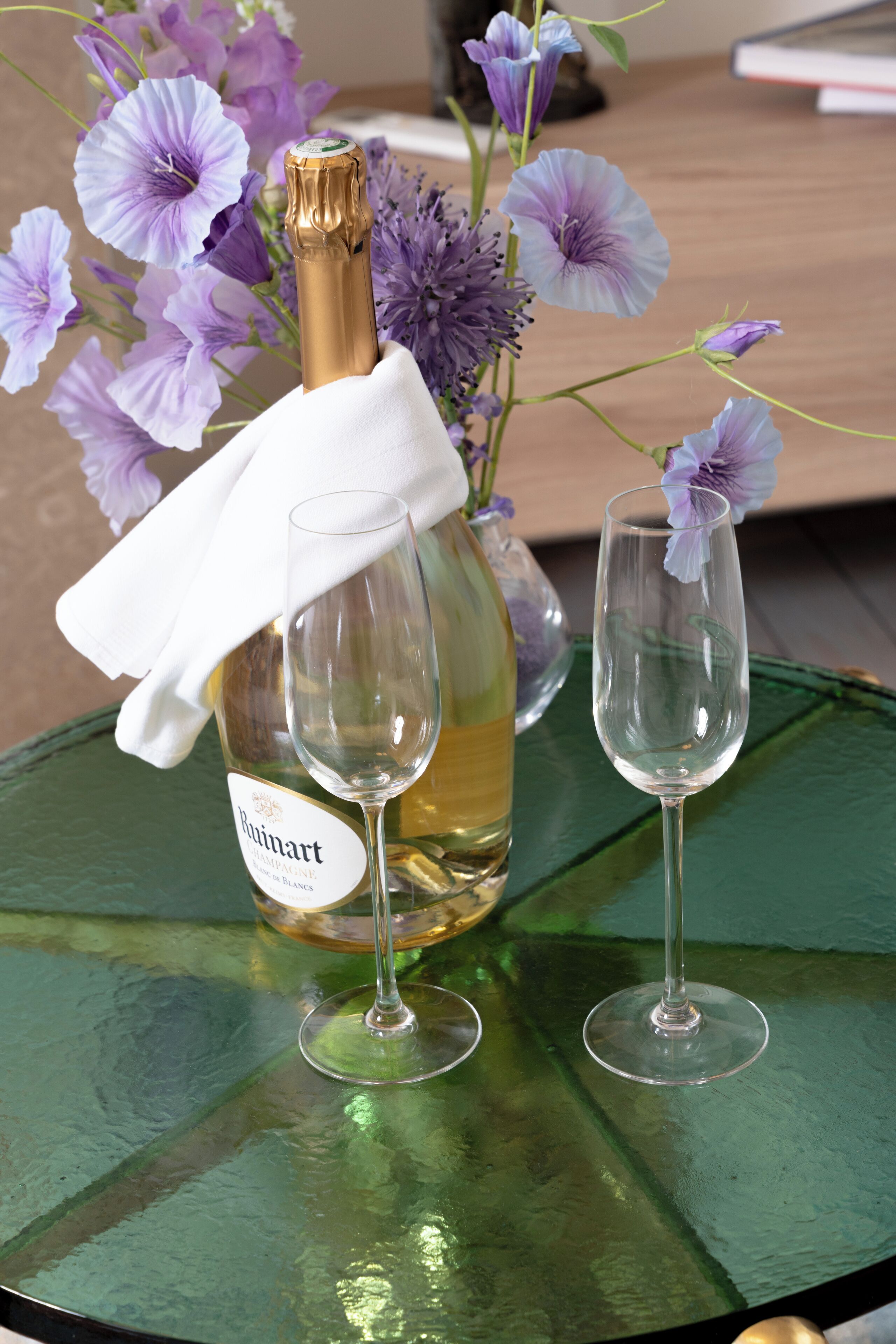 Een fles Buvart champagne, een glas en een glas water op een groene tafel met paarse bloemen.