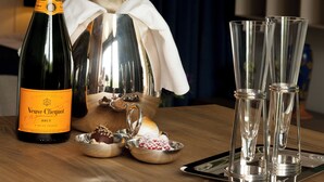 A bottle of Veuve Clicquot champagne, a silver charger set, and four champagne flutes on a wooden table in a hotel room. - Suite Aux Anges (Antwerp)