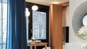 A modern living room with a white sofa, a blue pillow, and a dining area with a wooden table and chairs. - Suite Aux Anges (Antwerp)