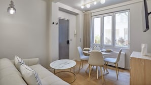 Una sala moderna con sofá, mesa de comedor y sillas. Hay una ventana con cortinas, una puerta y una lámpara en el techo.