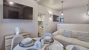 Una sala de estar moderna con sofá, mesa de comedor dispuesta con platos y vasos, televisor de pantalla plana montado en la pared e iluminación colgante.